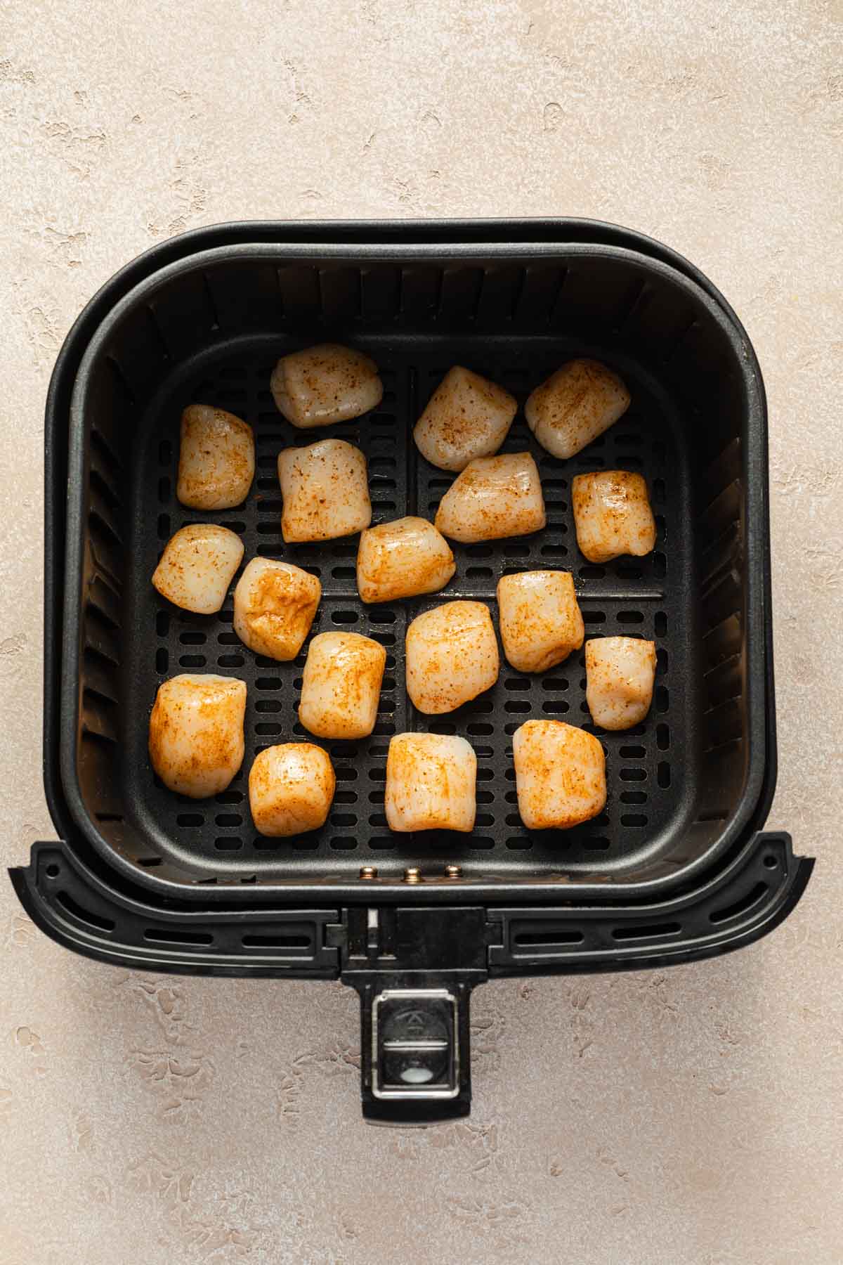 Scallops arranged in a single layer in an air fryer basket.