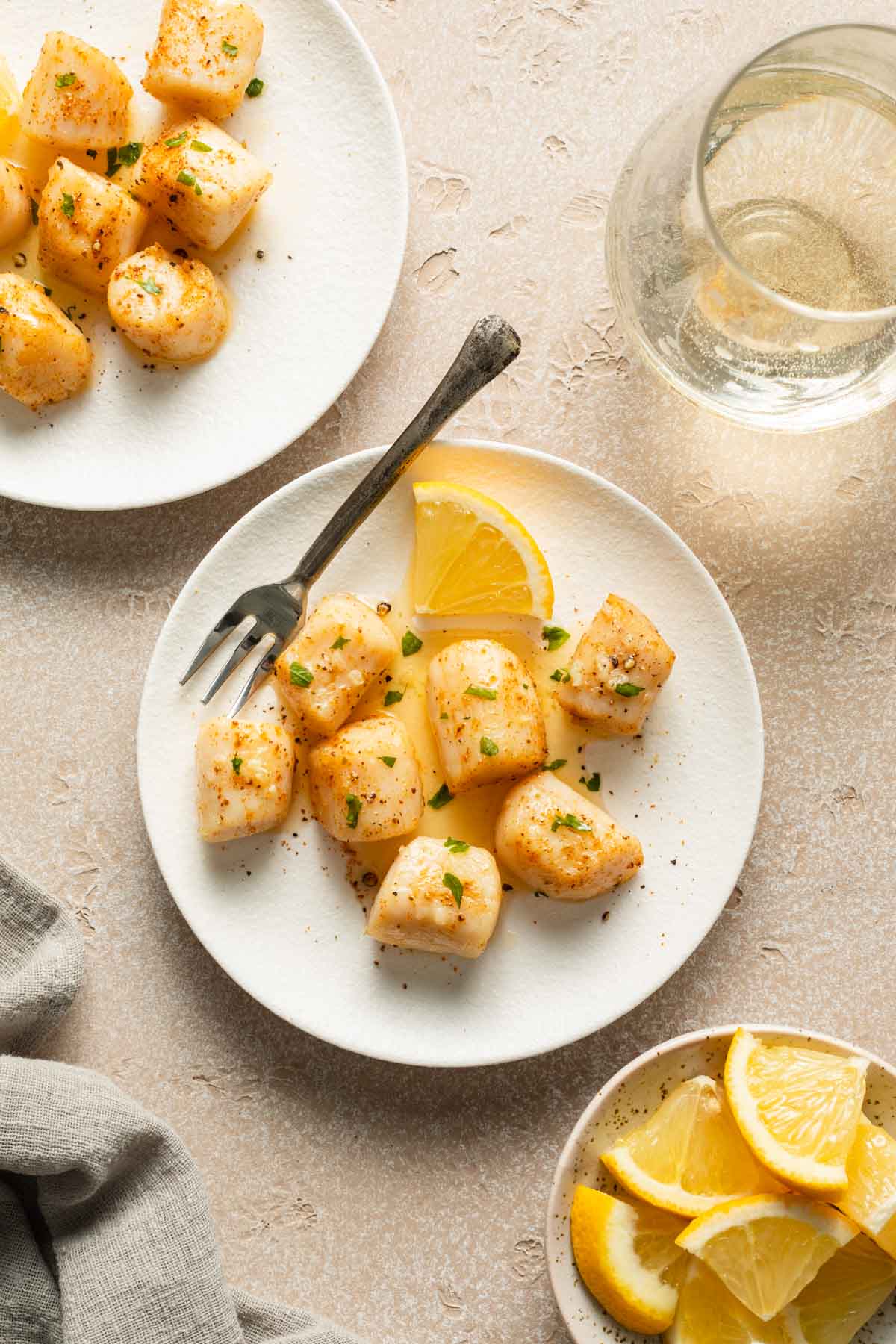 Air fried scallops arranged on two white plates next to lemon wedges and a glass of wine.