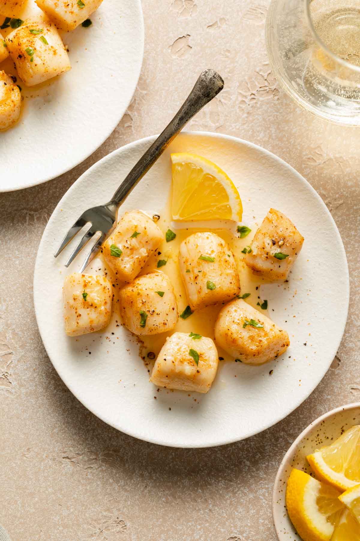 Scallops topped with melted butter and chopped parsley on a white plate.