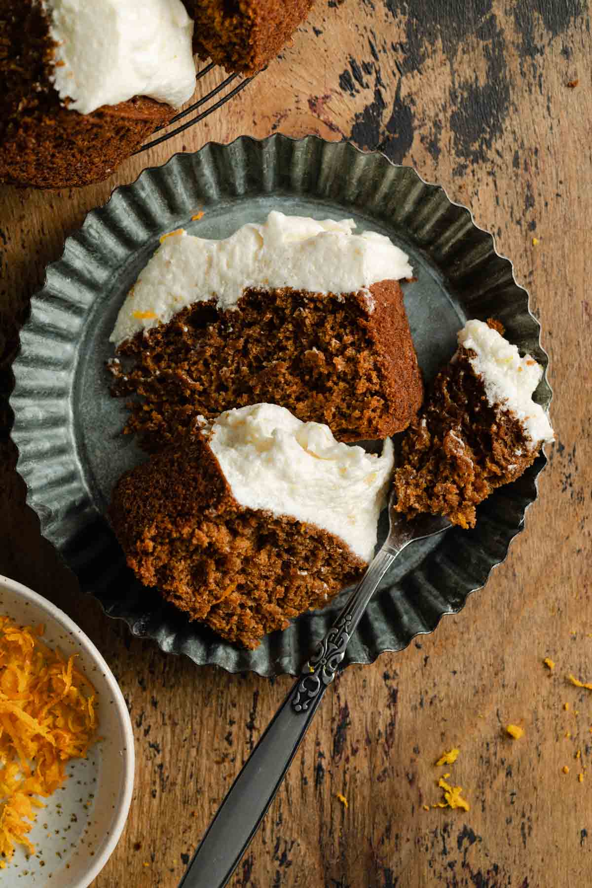 Two pieces of orange spice cake on a ruffled tin plate with a fork.