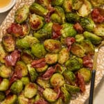 Roasted Brussels sprouts with prosciutto served on a platter with a serving spoon.