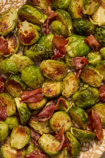 Roasted Brussels sprouts with prosciutto served on a platter with a serving spoon.
