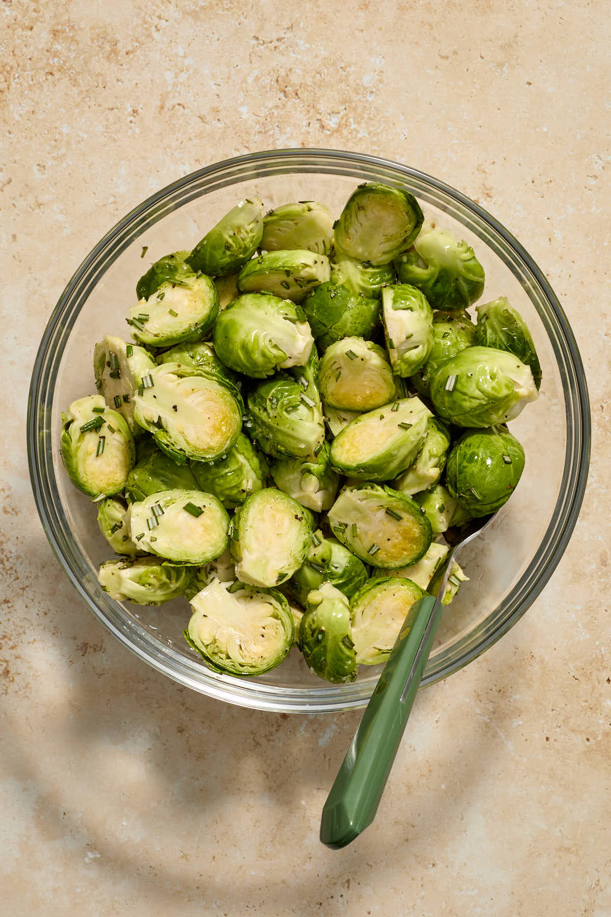 Trimmed and halved Brussels sprouts in a glass bowl and tossed with oil and seasonings.