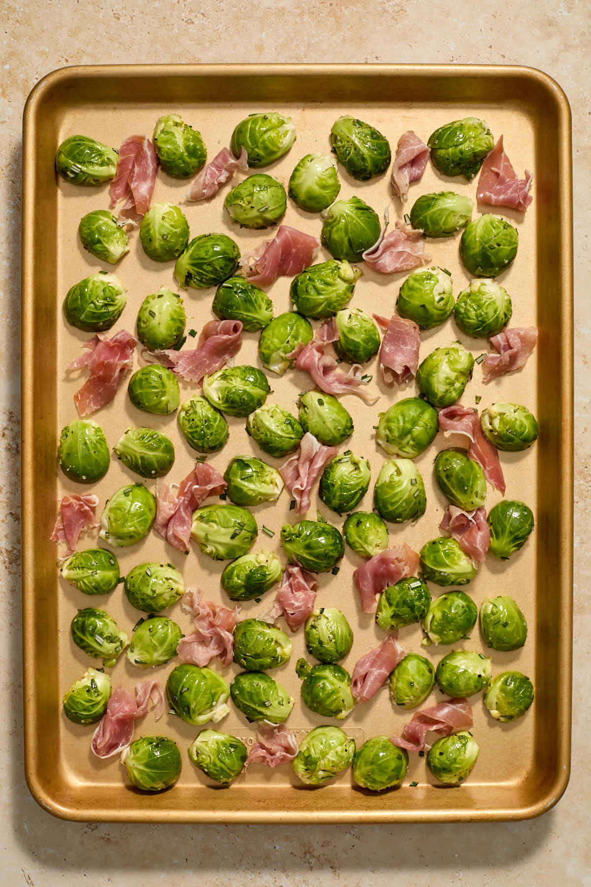 Torn pieces of prosciutto arranged around the Brussels sprouts on a sheet pan.