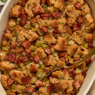 Whole wheat sausage stuffing in a baking dish with a serving spoon and chopped parsley on top.