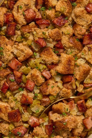 Whole wheat sausage stuffing in a baking dish with a serving spoon and chopped parsley on top.