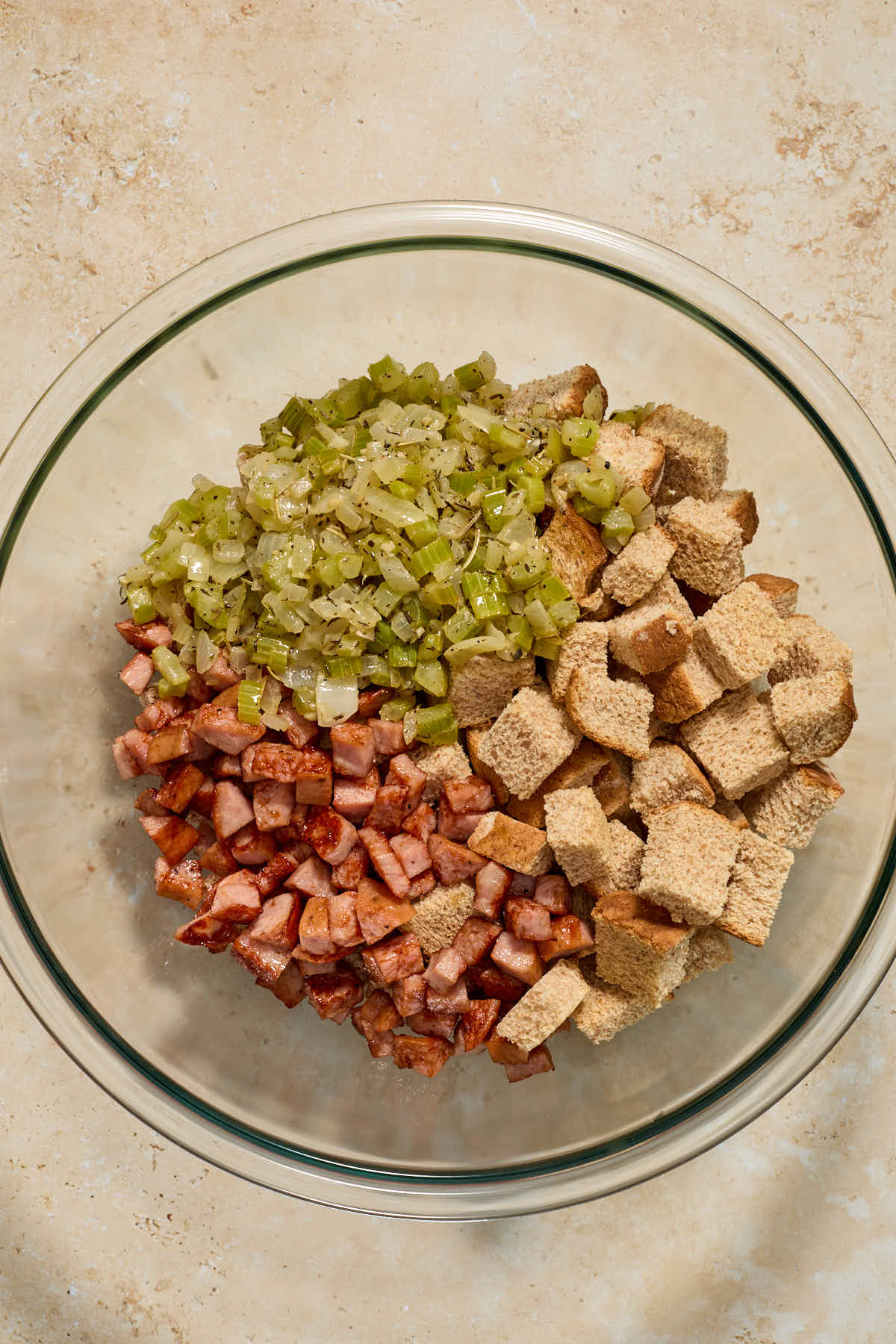 Bread cubes, sausage and vegetable/herb mixture added to a large glass bowl.