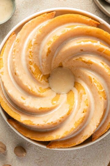 Overhead view of an eggnog bundt cake topped with glaze on a round plate.