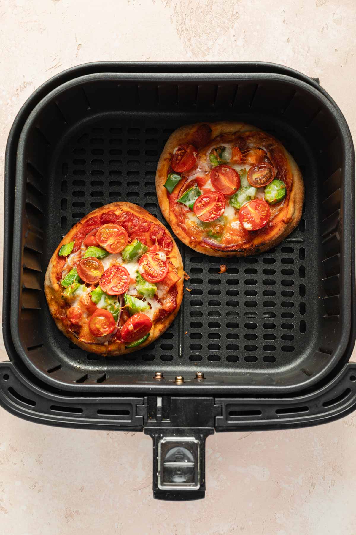 Two mini pizzas in an air fryer basket.