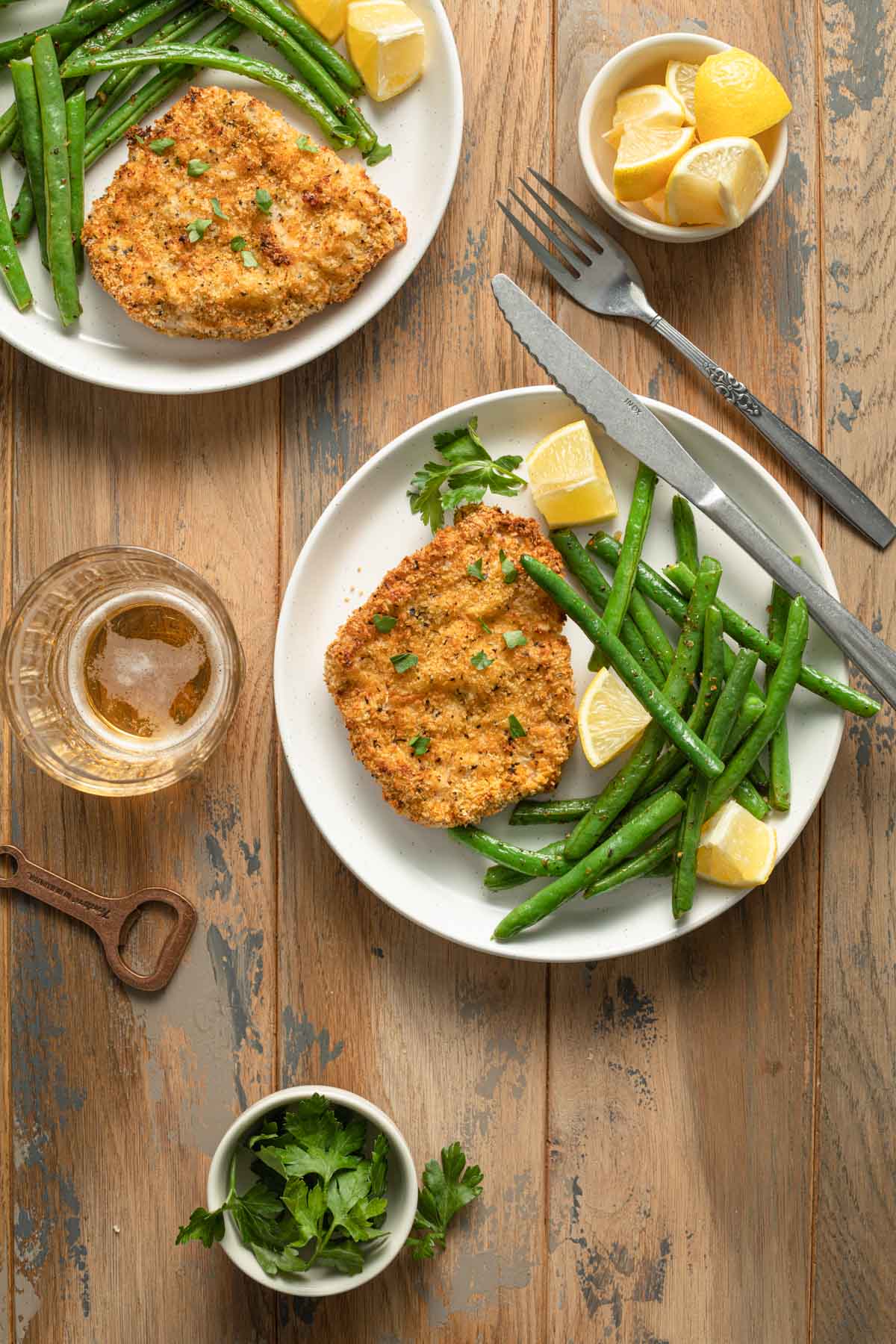 Pork schnitzel on white plates and served with green beans and lemon wedges.