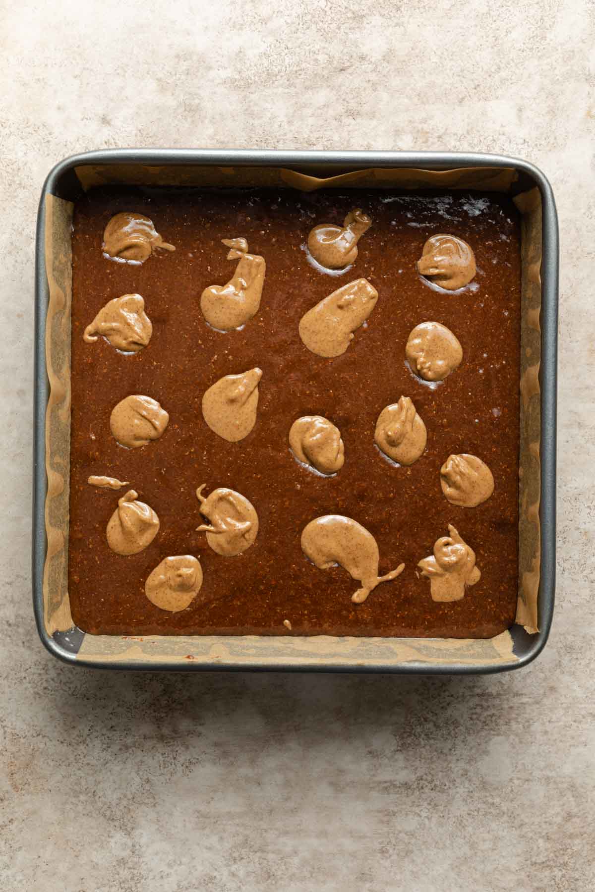 Brownie batter in a pan with dollops of almond butter on top.