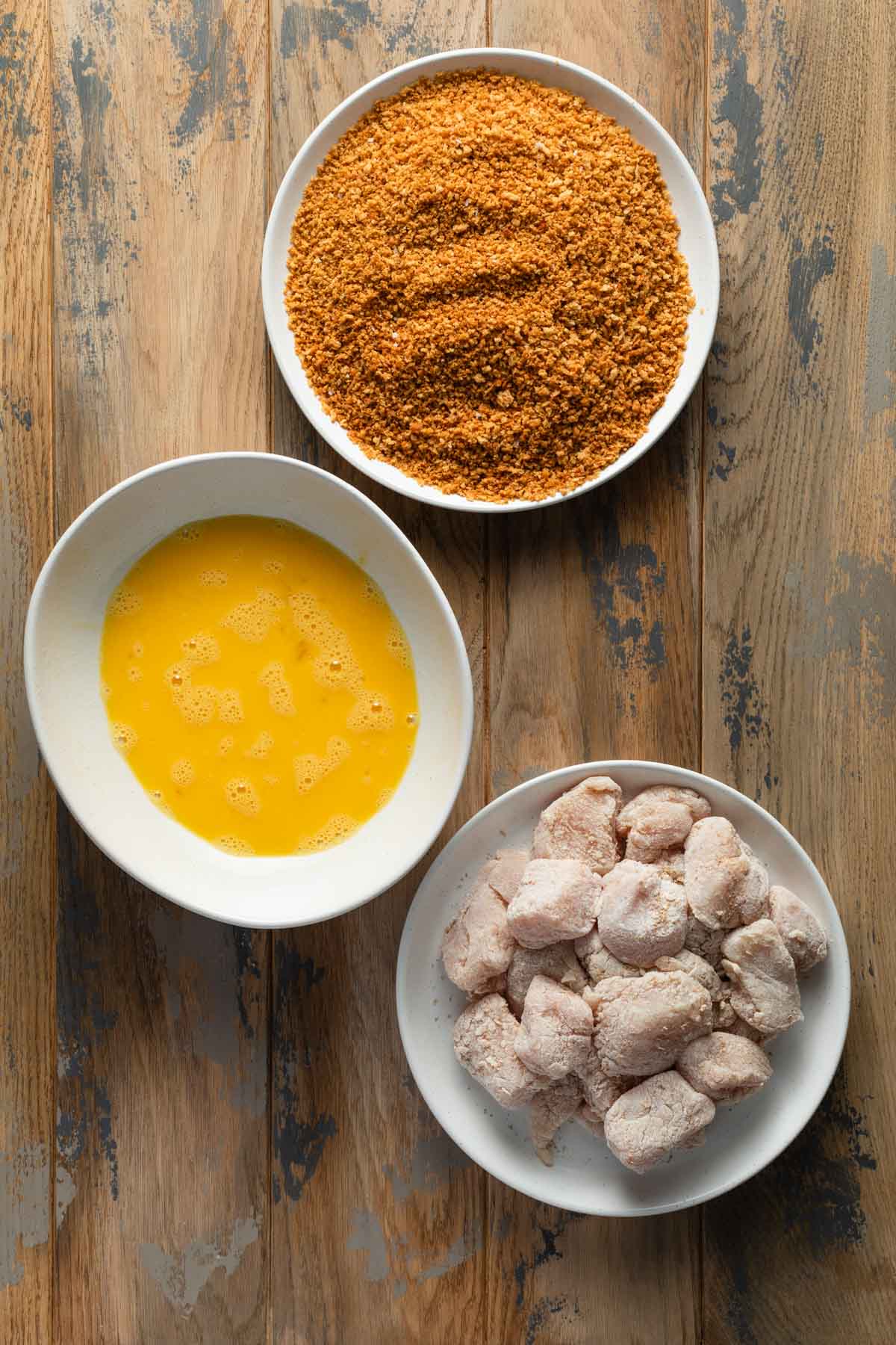 Floured chicken, whisked eggs and panko seasoning arranged in separate dishes.