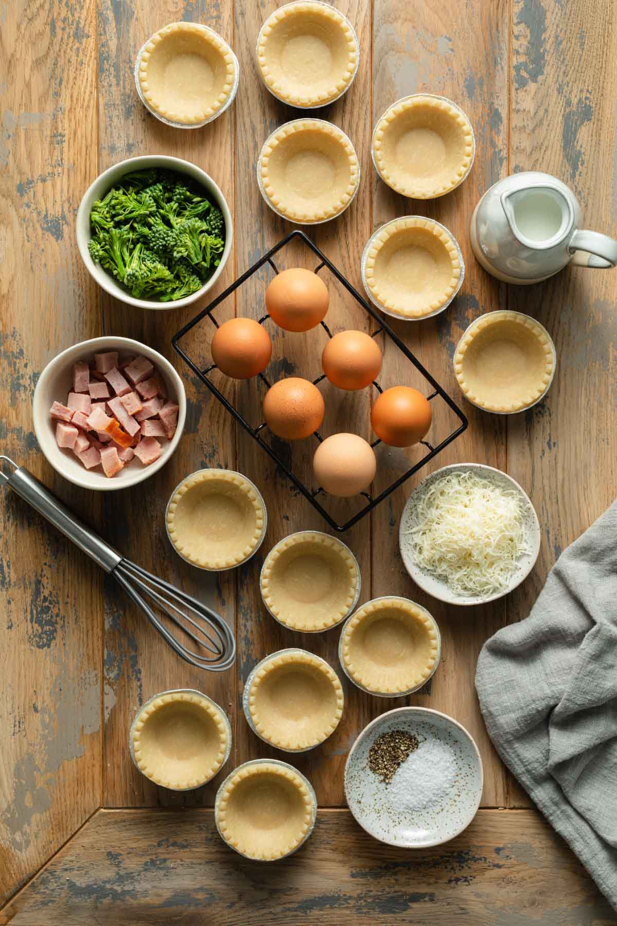 Ingredients to make air fryer quiche arranged individually on a wooden surface.