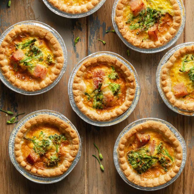 Mini quiche in tart shells arranged on a wooden surface.