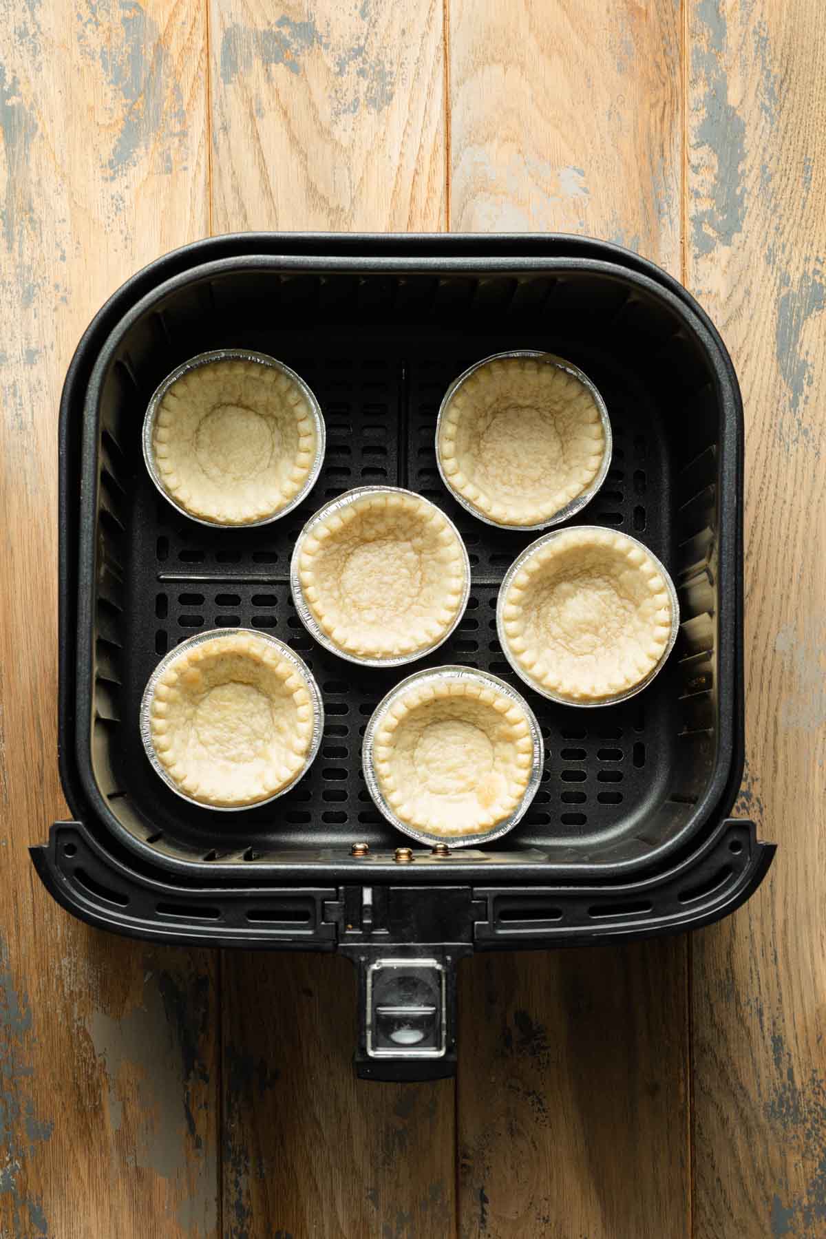 Par-baked mini tart shells in an air fryer basket.
