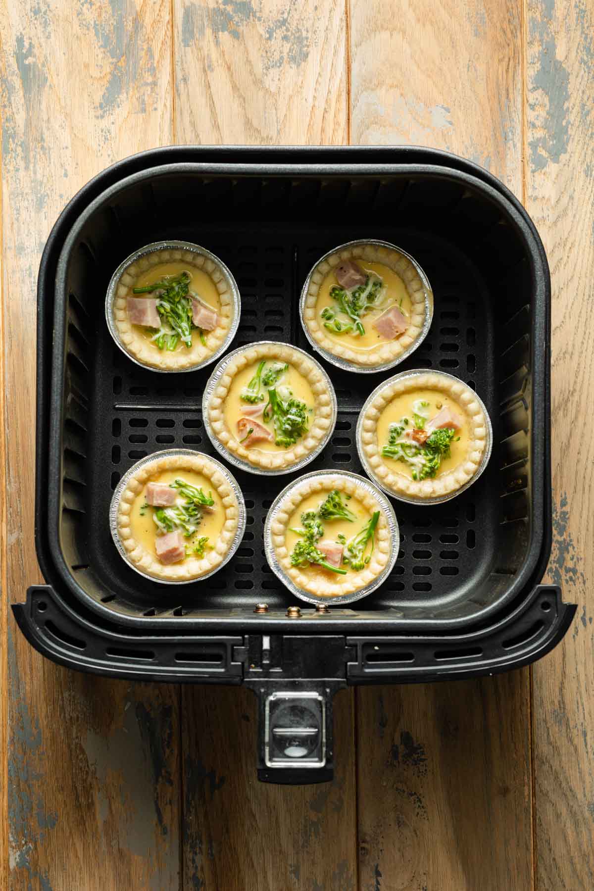 Par-baked tart shells filled with quiche filling in an air fryer basket.