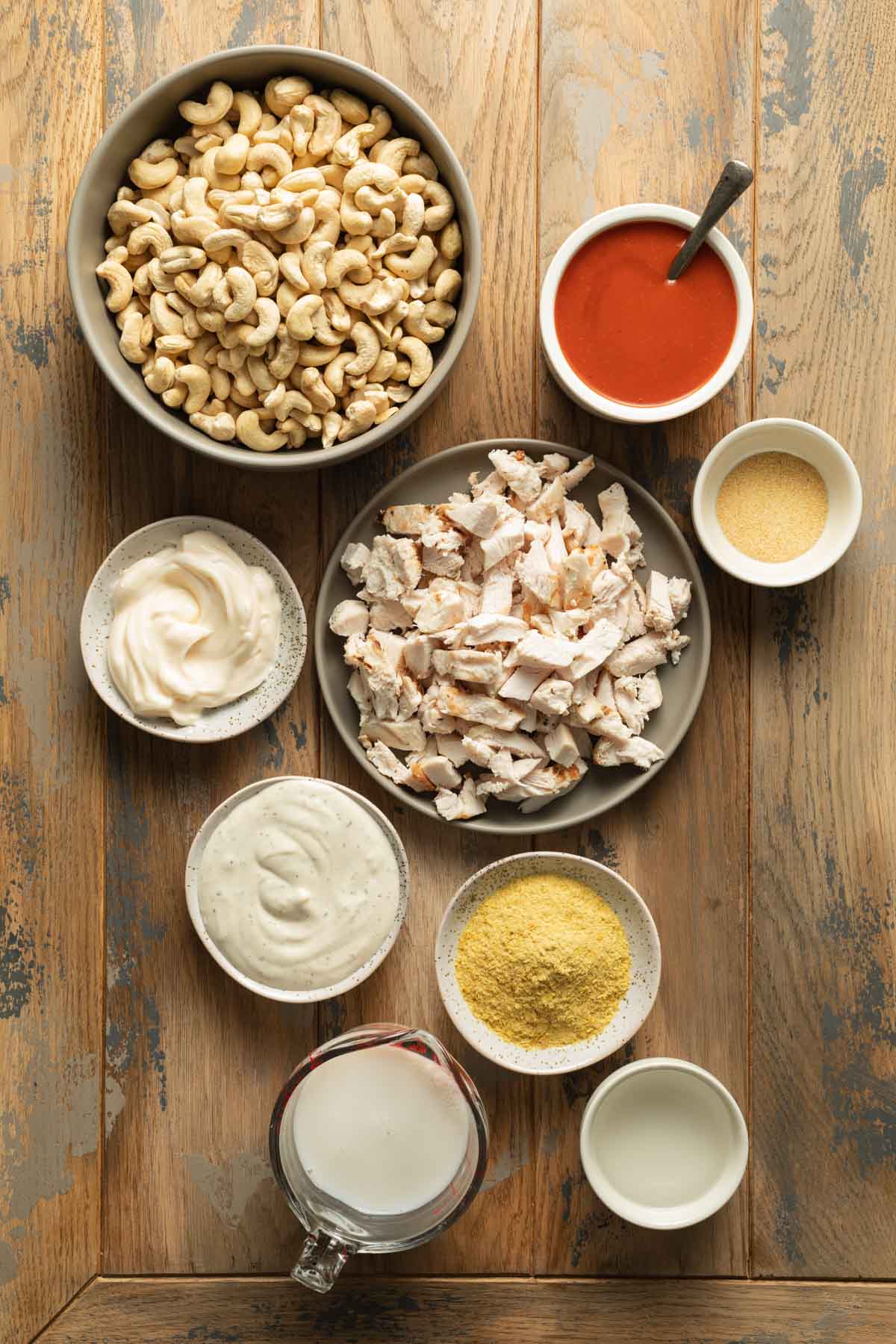 Ingredients to make buffalo chicken dip arranged individually on a wooden surface.
