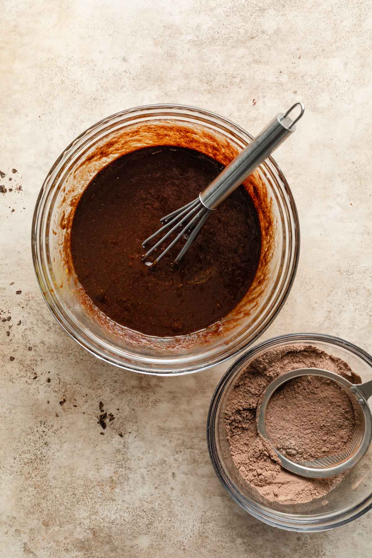 Wet chocolate mixture in a glass bowl next to a bowl of dry ingredients.