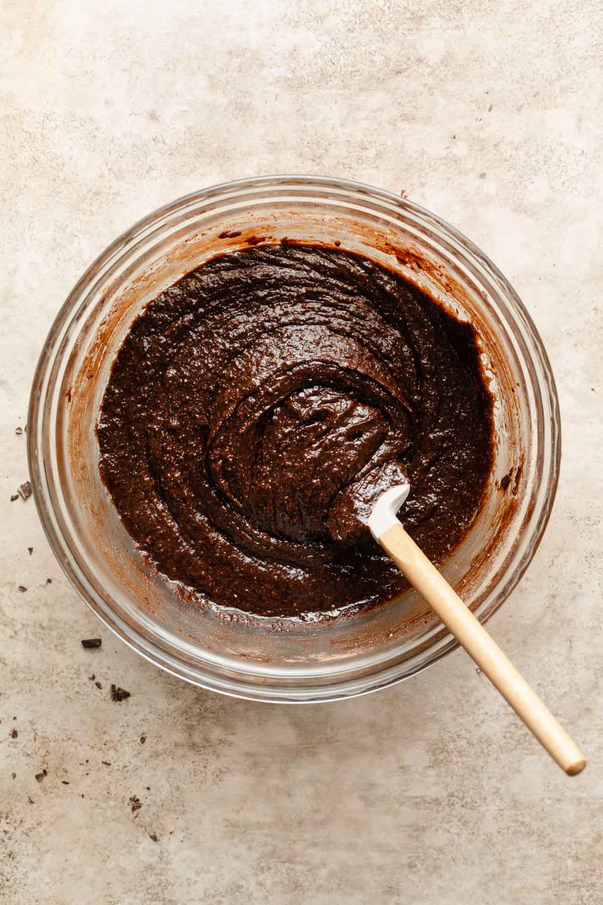 Brownie batter in a glass bowl with a spatula inserted into it.