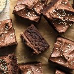 Frosted tahini brownies cut into squares and arranged on a sheet of brown parchment paper.