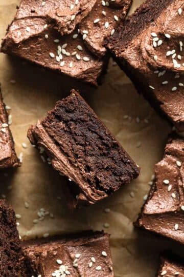 Frosted tahini brownies cut into squares and arranged on a sheet of brown parchment paper.