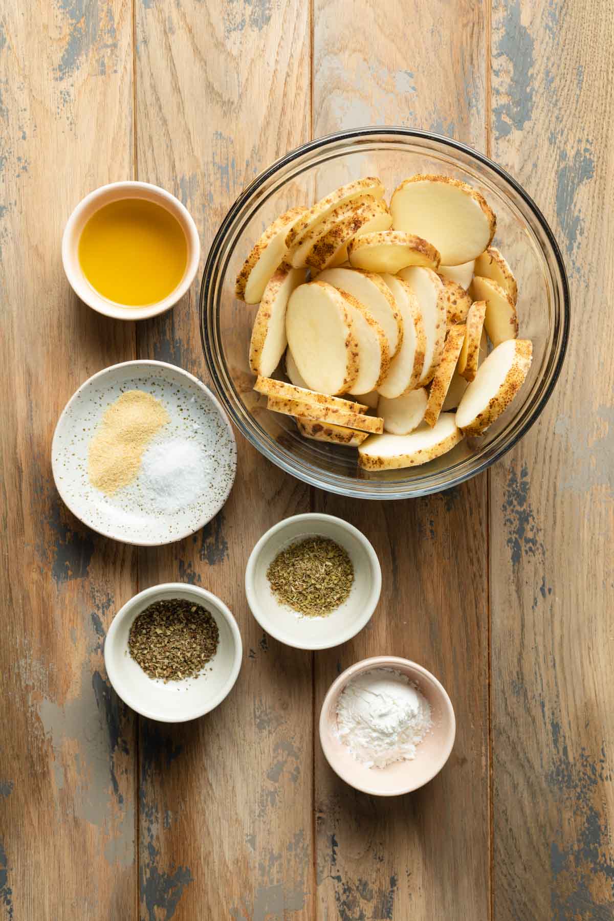 Ingredients to make air fryer potato slices arranged individually on a wooden surface.