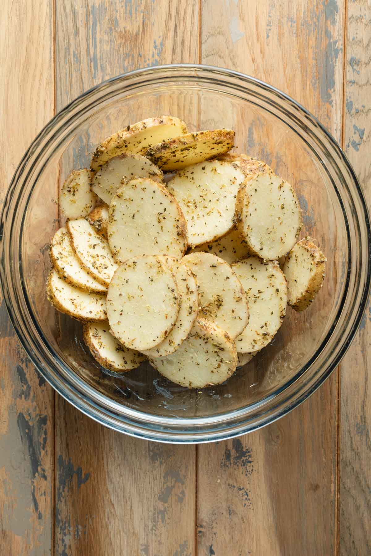 Seasoned potato slices in a large glass bowl.
