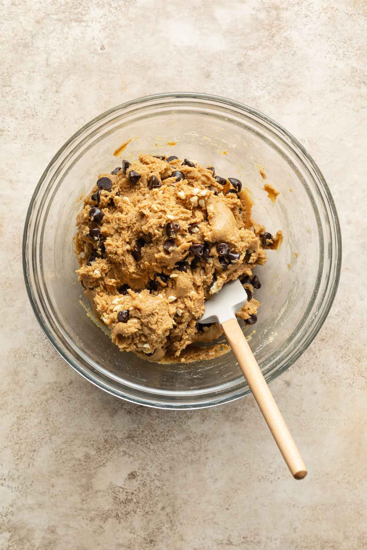 Cookie dough mixed with chocolate chips and peanuts in a glass bowl.
