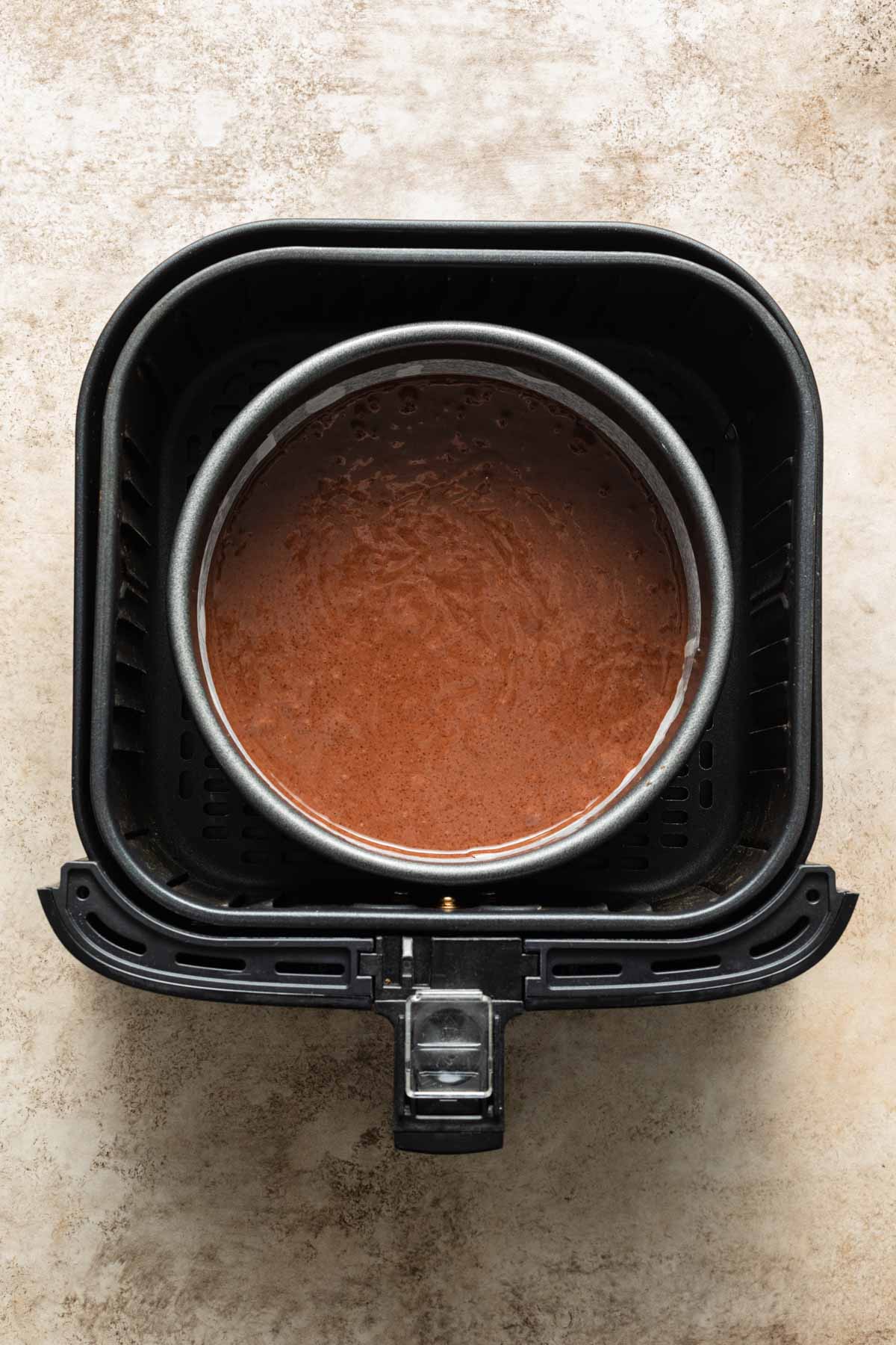 Overhead view of chocolate cake batter in a round pan inside an air fryer basket.