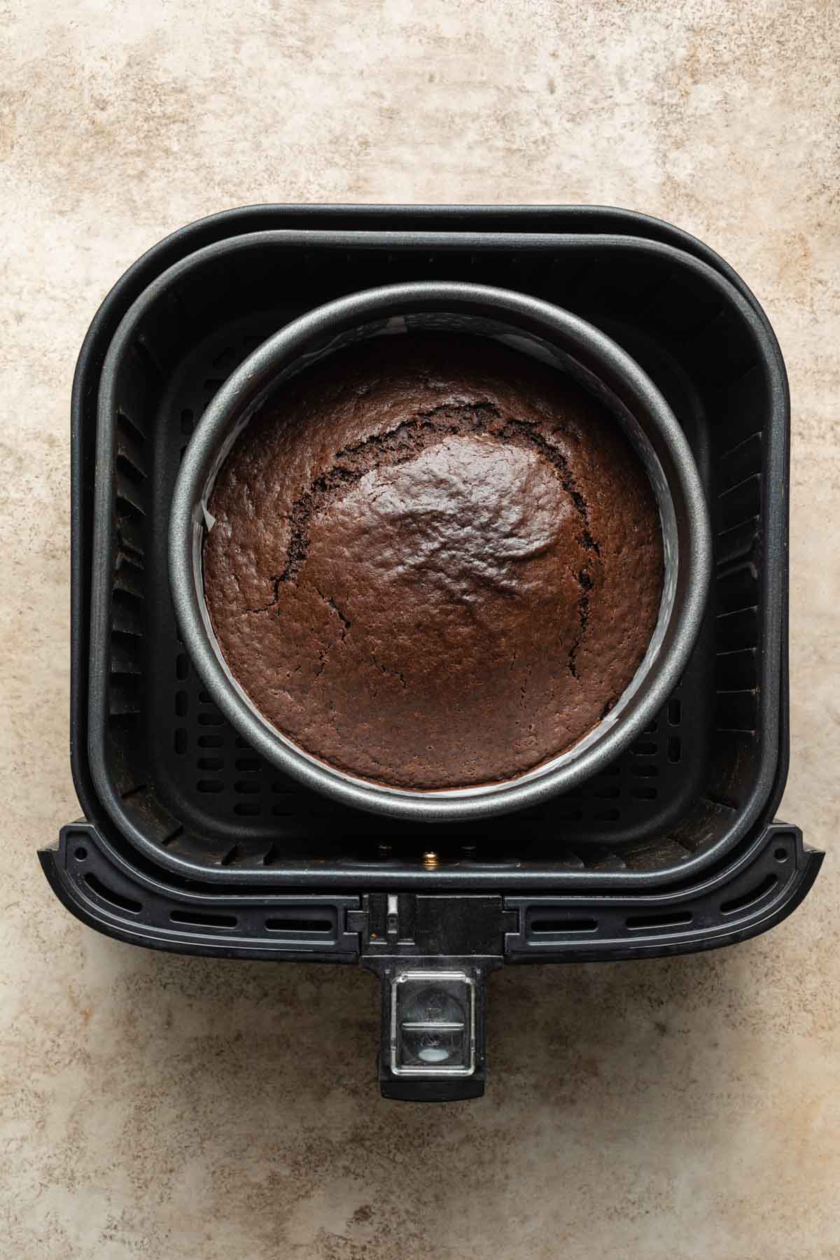 Overhead view of a baked chocolate cake in a round pan inside an air fryer basket.