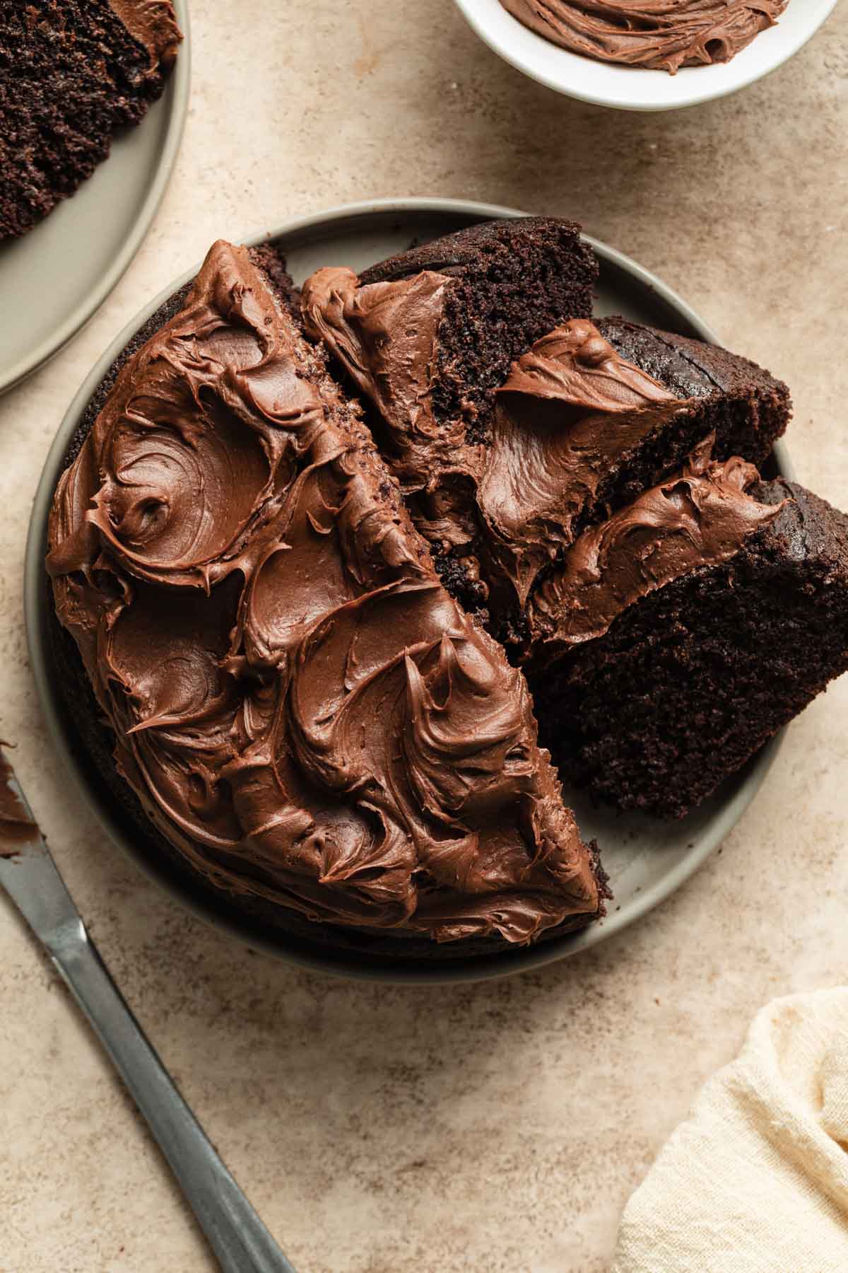 Overhead view of chocolate cake on a serving plate with half of the cake sliced into pieces.