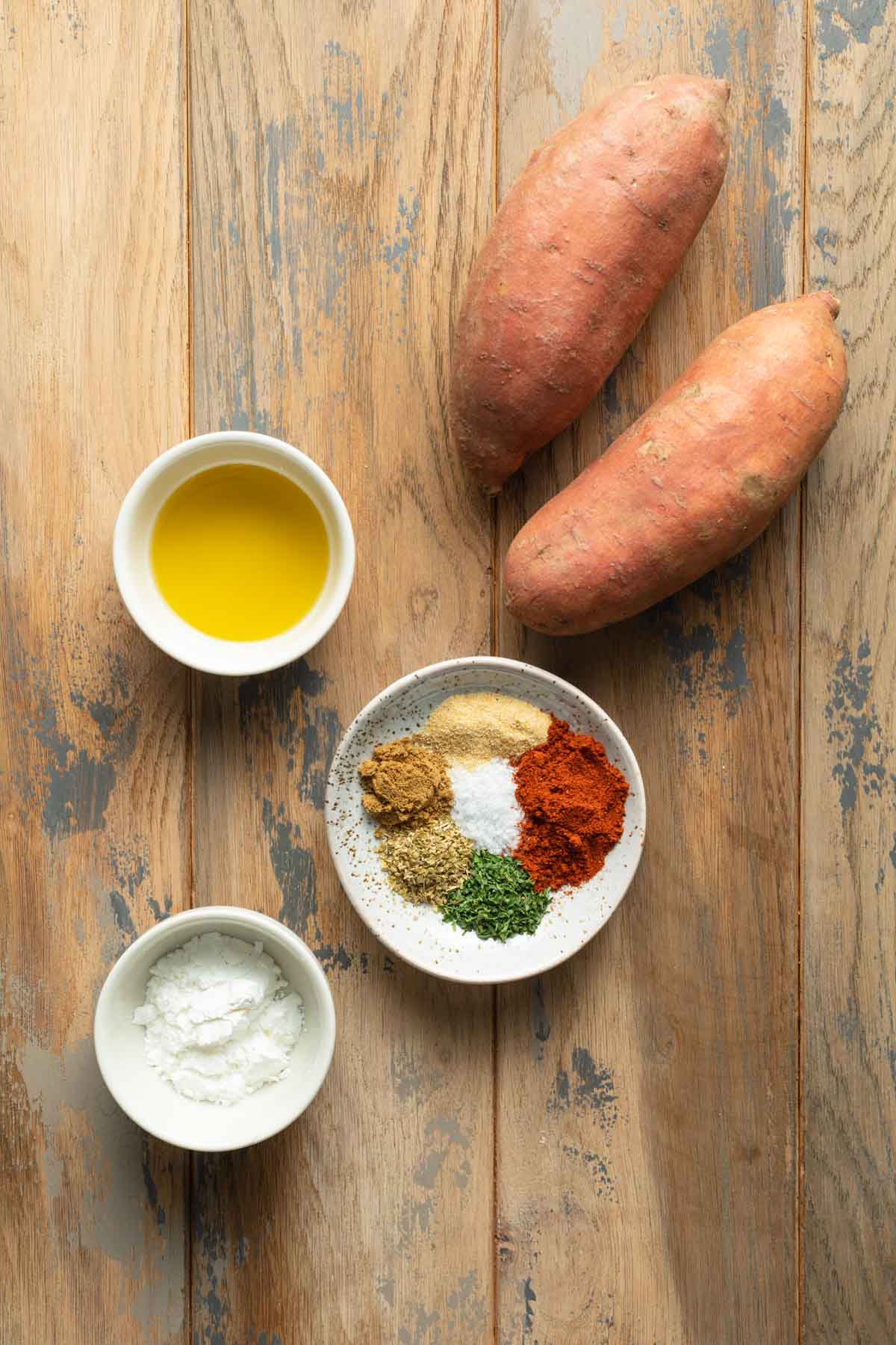 Ingredients to make air fryer sweet potato wedges arranged individually on a wooden surface.