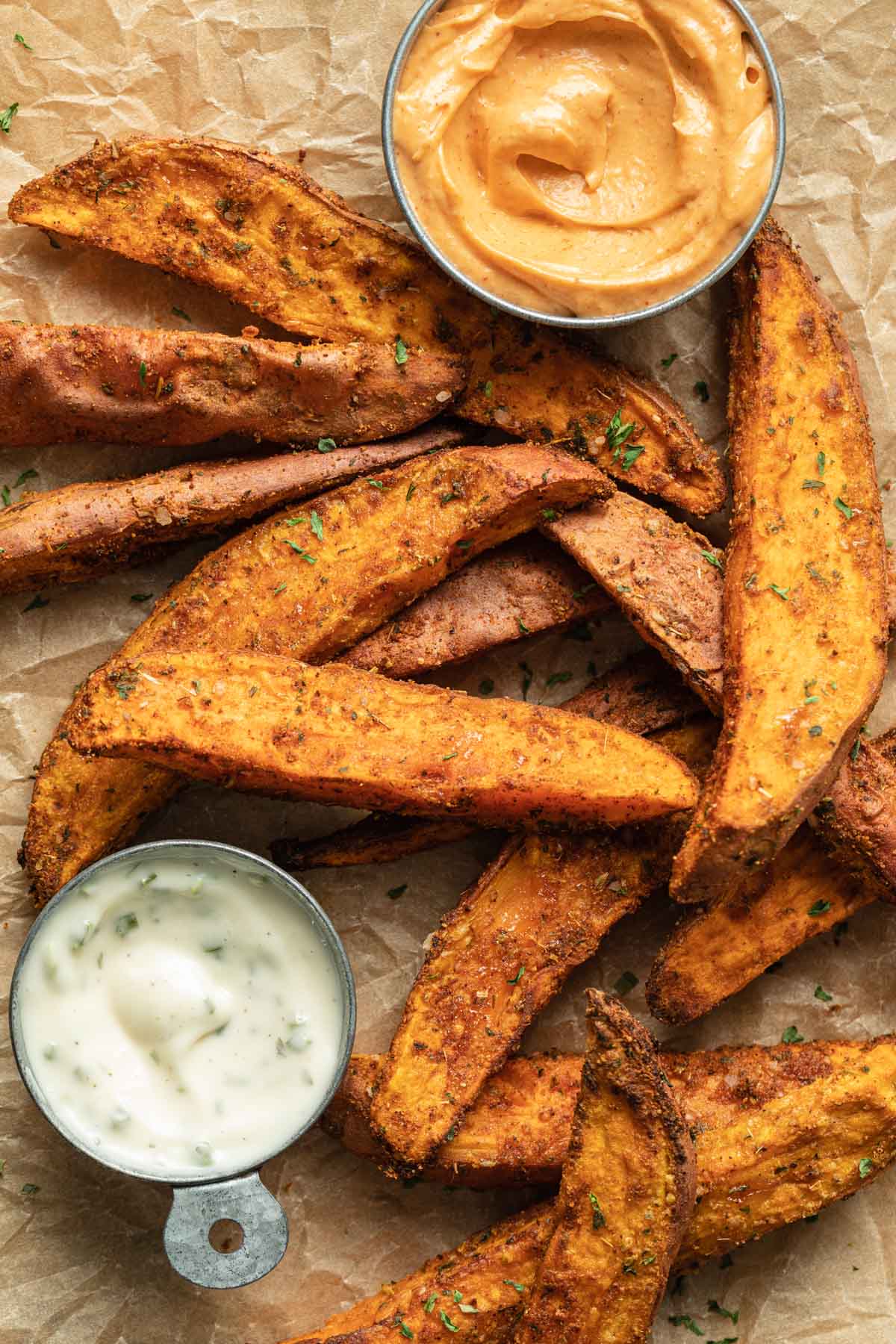 Air fryer sweet potato wedges arranged on parchment paper with a side of ranch dip.