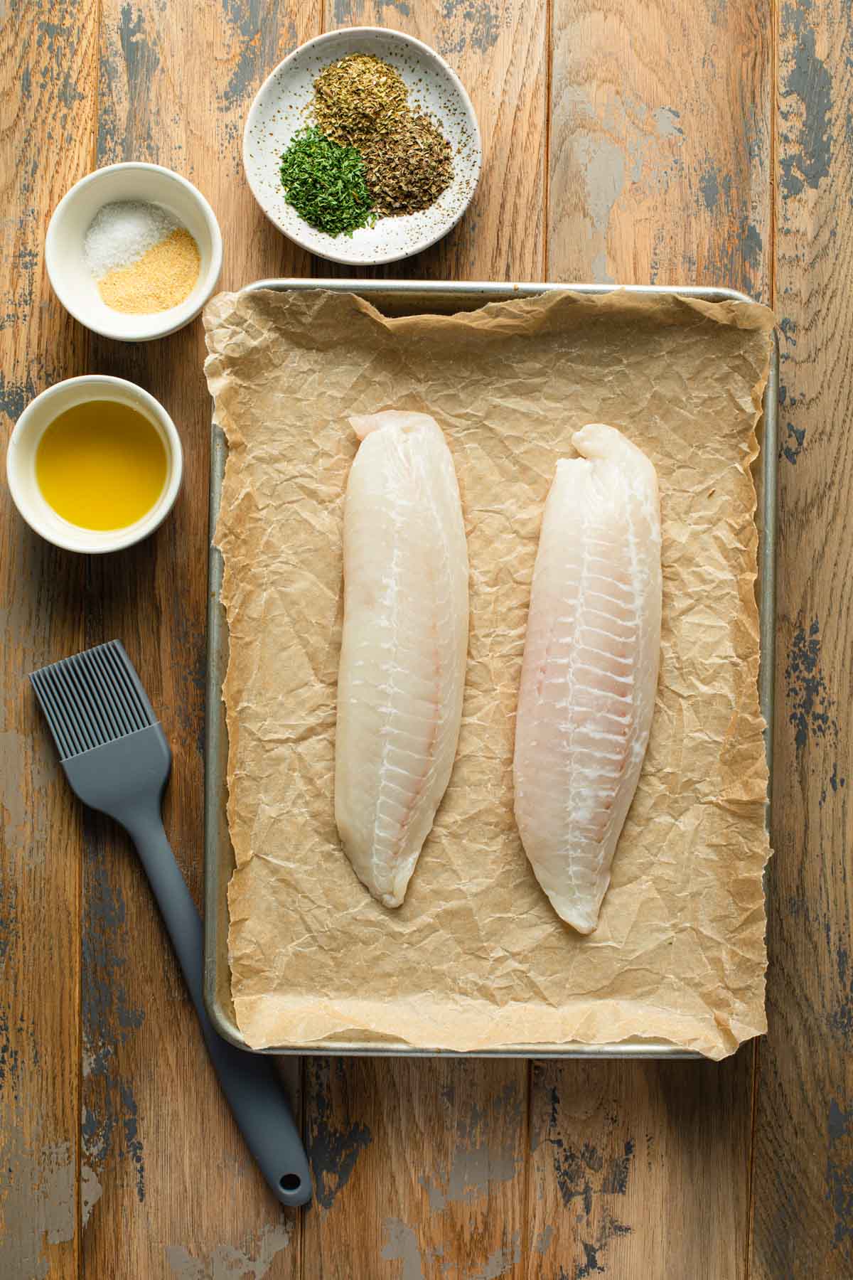 Ingredients to make air fryer tilapia arranged on a wooden table surface.