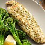 Close up view of a piece of air fryer tilapia on a plate with roasted broccoli.