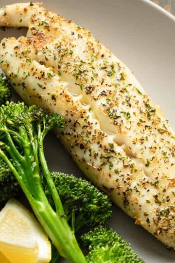 Close up view of a piece of air fryer tilapia on a plate with roasted broccoli.