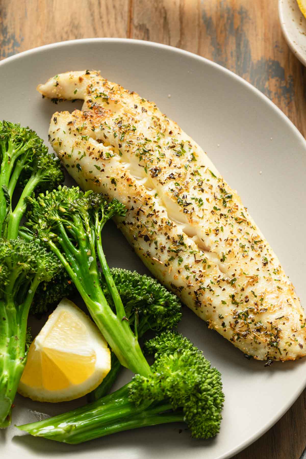 Close up view of a piece of air fried tilapia on a plate with broccoli.