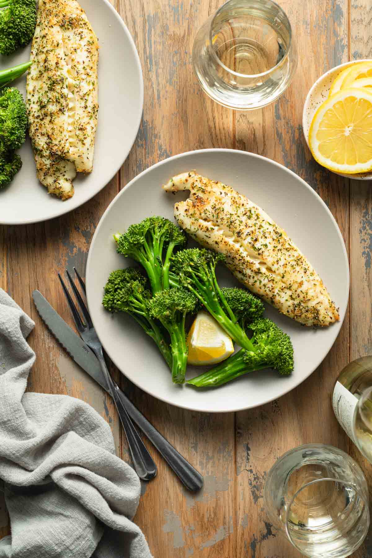 Two plates of tilapia and roasted broccoli arranged on a table.