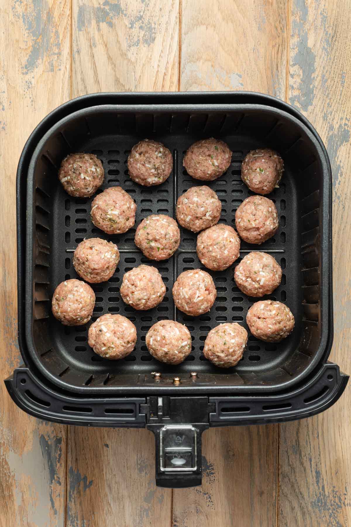 Uncooked meatballs in an air fryer basket.