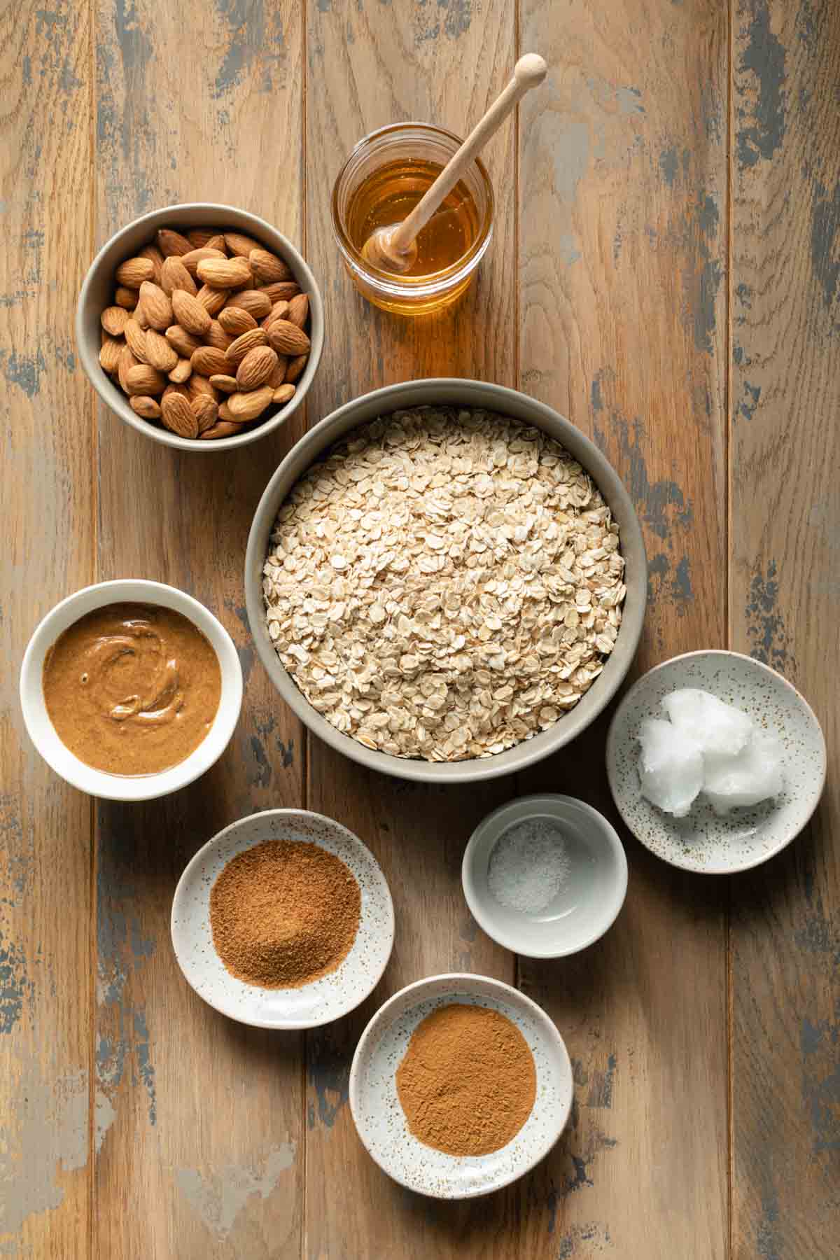 Ingredients to make honey almond granola arranged individually on a wooden table surface.