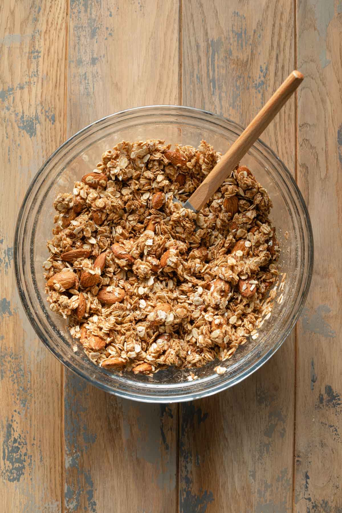 Wet granola mixture in a glass bowl with a spatula.