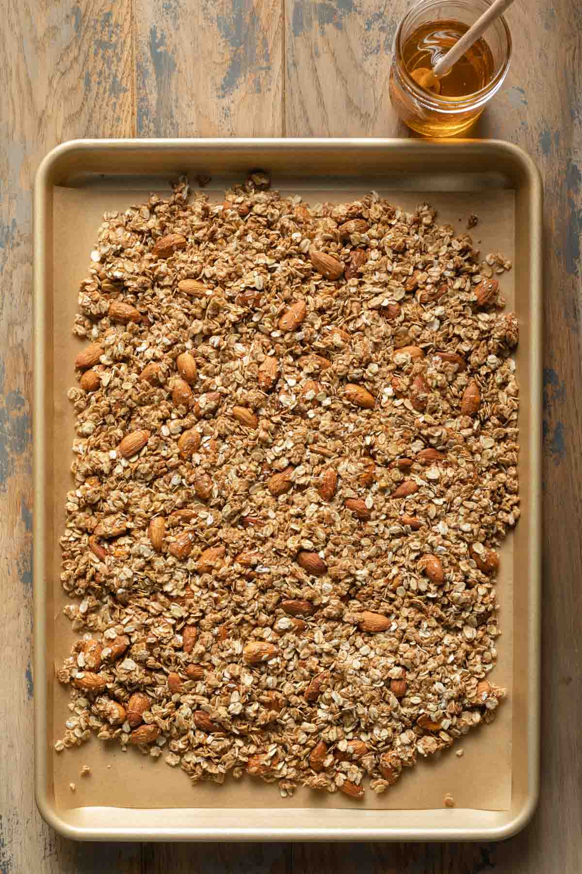 Granola mixture spread out on a parchment paper lined baking sheet.