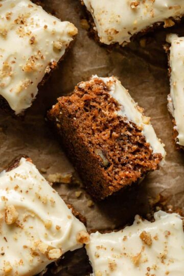 Pieces of carrot cake arranged on parchment paper with a piece turned on its side.