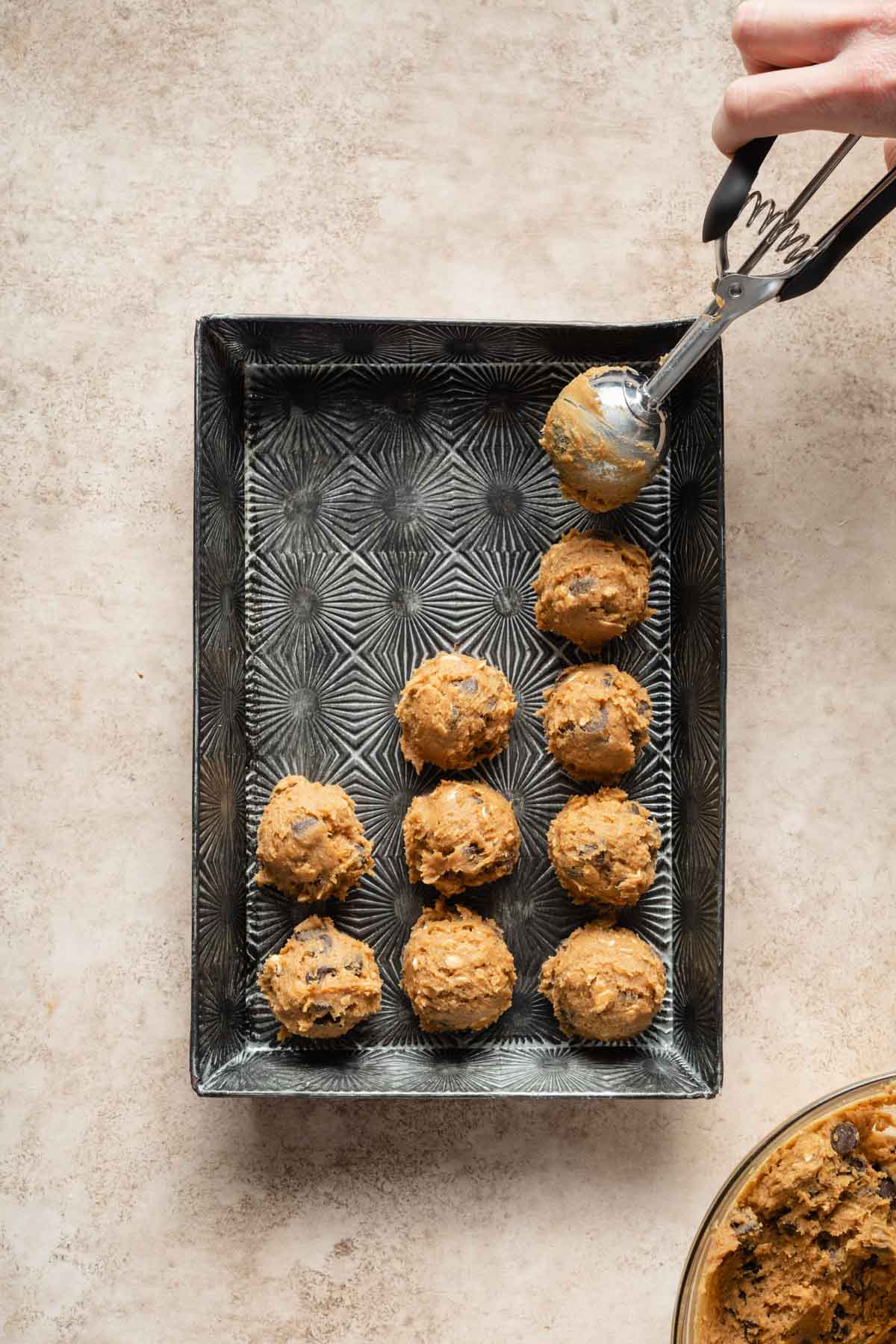 Cookie dough balls being scooped onto a tray.