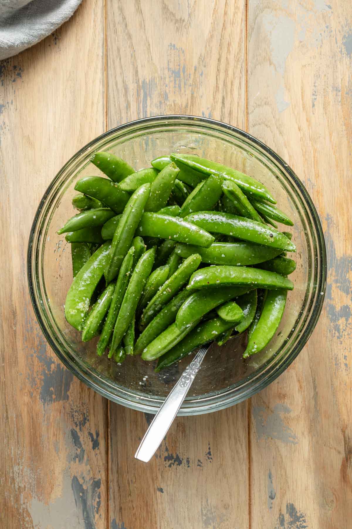 Snap peas in a glass bowl and coated with oil and seasonings.