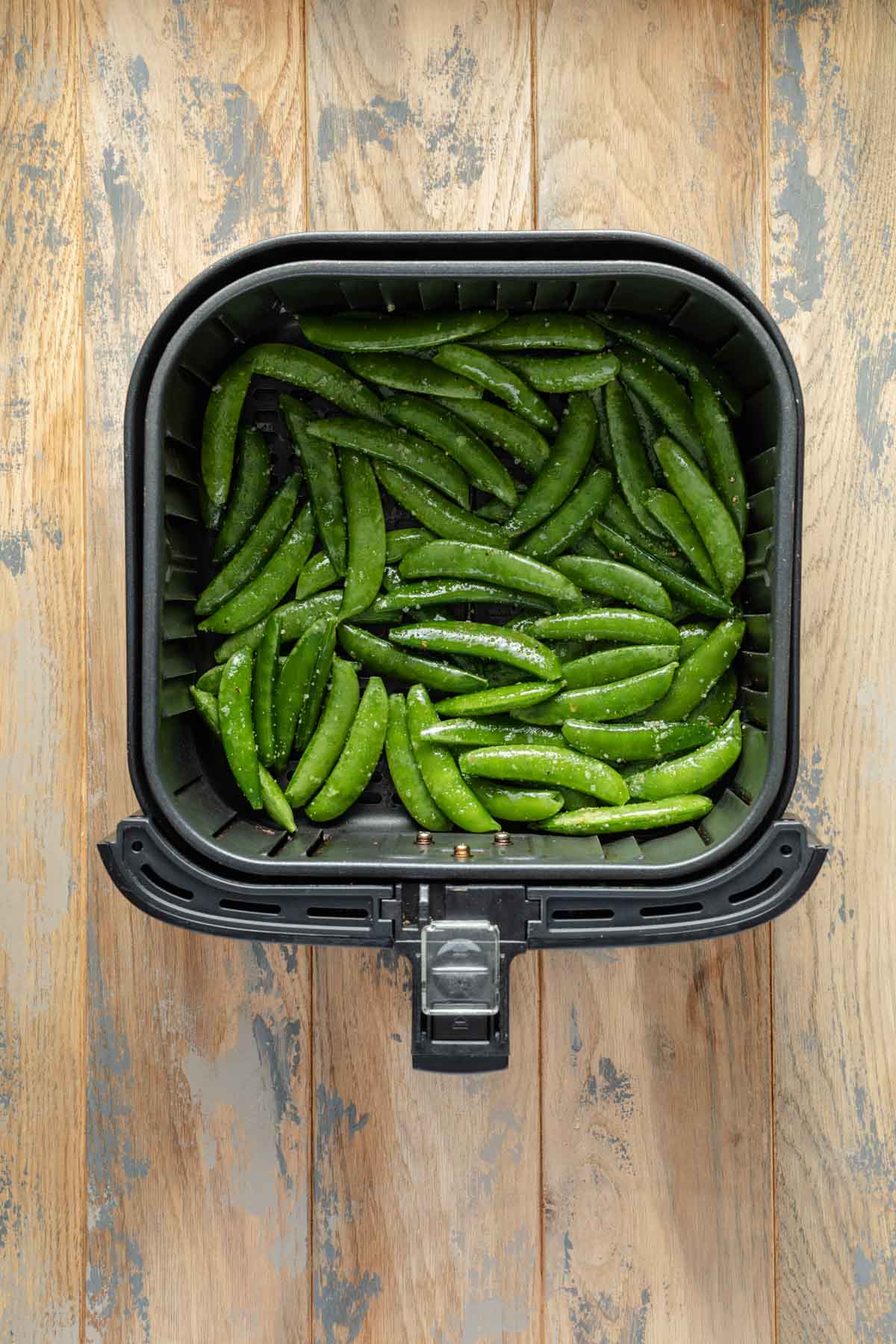 Seasoned snap peas in an air fryer basket.