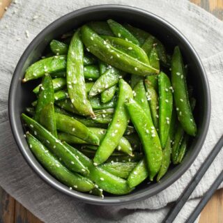 Overhead view of air fryer snap peas in a black bowl on top of a grey napkin.