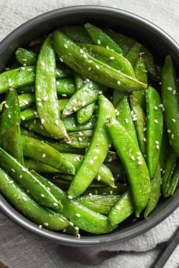 Overhead view of air fryer snap peas in a black bowl on top of a grey napkin.