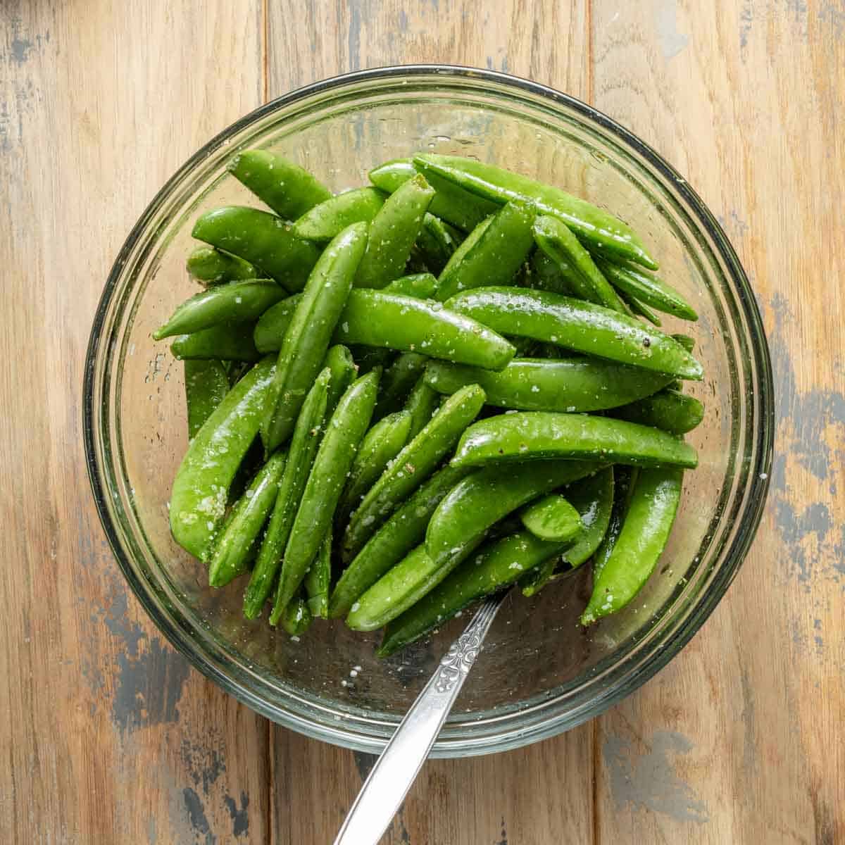 Snap peas in bowl mixed with oil and seasonings.
