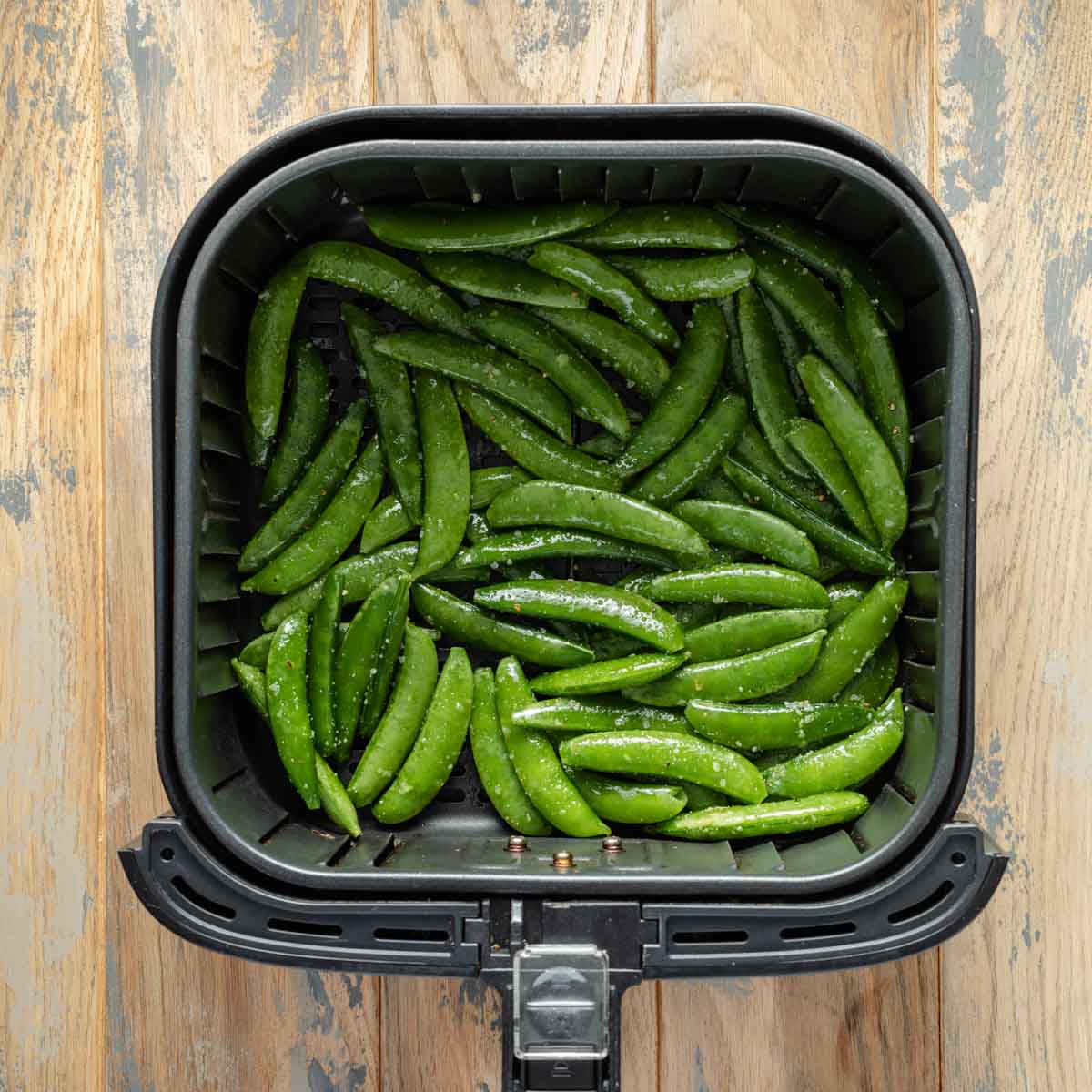 Raw and seasoned snap peas in air fryer basket.